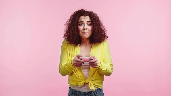 KIEW, UKRAINE - 30. JUNI 2021: Besorgte Frau mit Steuerknüppel und Videospiel isoliert auf rosa — Stockfoto