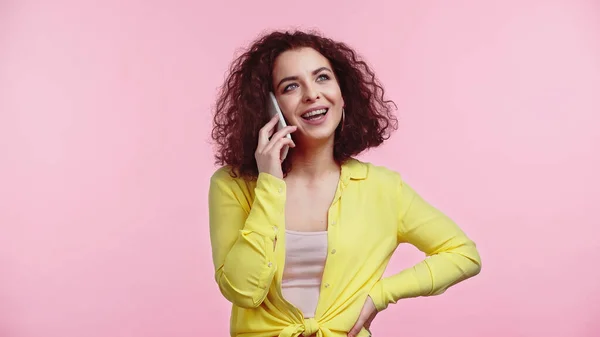 Щаслива жінка стоїть з рукою на стегні, розмовляючи на мобільному телефоні ізольовано на рожевому — стокове фото
