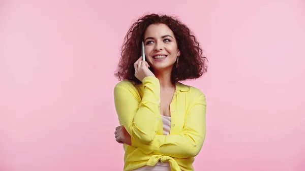 Pleased young woman standing while talking on cellphone isolated on pink — Stock Photo