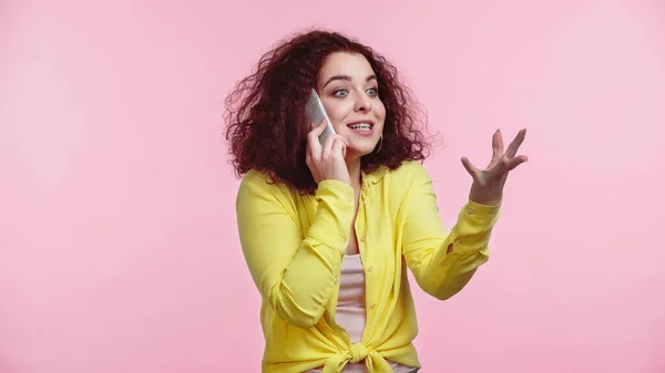 Junge fröhliche Frau gestikuliert, während sie auf dem Smartphone spricht, isoliert auf rosa — Stockfoto