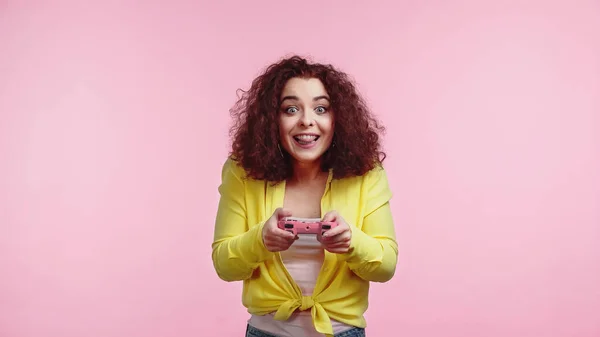 КИІВ, УКРАЇН - 30 ЧЕРВНЯ 2021 року: добра молода жінка, яка тримає джойстик і витискає язик, ізольований на рожевому — стокове фото