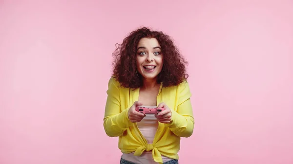 KYIV, UKRAINE - JUNE 30, 2021: positive young woman holding joystick and sticking out tongue isolated on pink — Stock Photo