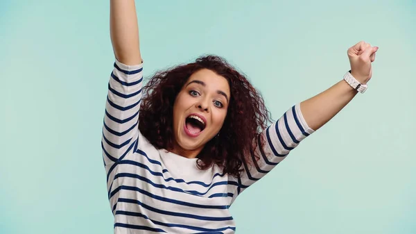 Excited young woman in striped long sleeve shirt with raised hands isolated on blue — Stock Photo