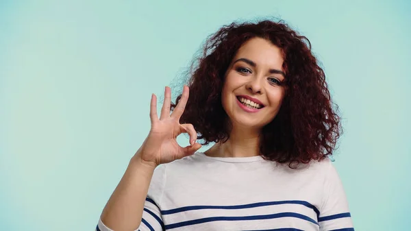 Happy young woman in striped long sleeve shirt showing ok sign isolated on blue — Stock Photo