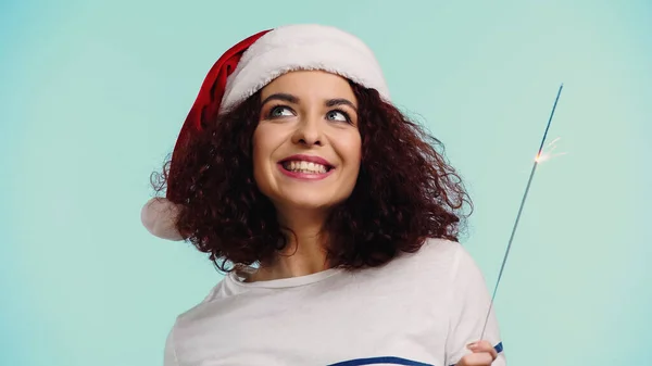 Happy woman in santa hat holding sparkler isolated on blue — Stock Photo