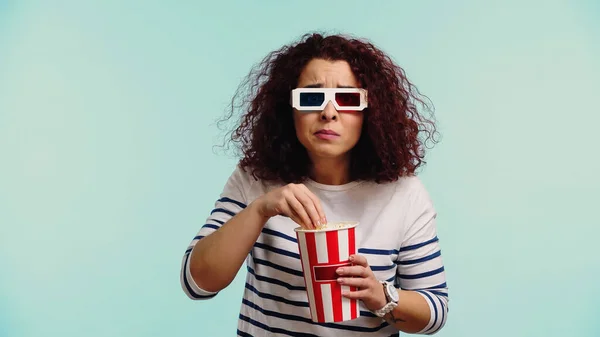 Femme bouclée dans des lunettes 3D avec seau de maïs soufflé regarder film isolé sur bleu — Photo de stock