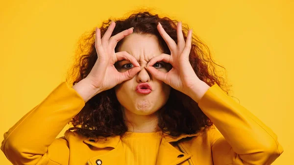 Кудрявая женщина имитирует очки с руками и гримасом изолированы на желтый — стоковое фото