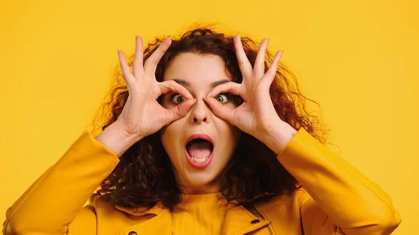 Donna scioccata imitando occhiali con le mani isolate su giallo — Foto stock