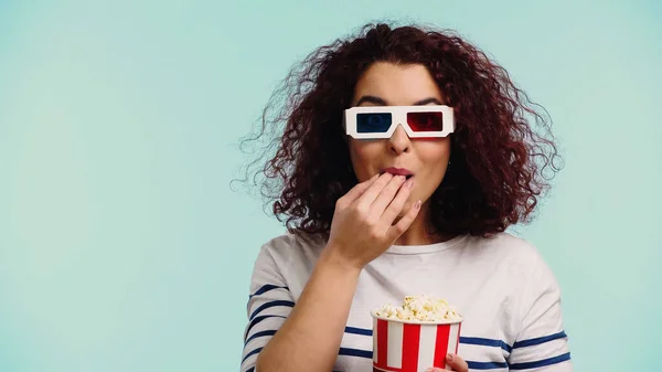 Junge Frau in 3D-Gläsern isst Popcorn und hält Eimer isoliert auf blauem Grund — Stockfoto