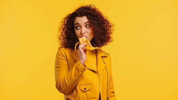 Mujer joven en chaqueta de cuero comiendo plátano aislado en amarillo - foto de stock