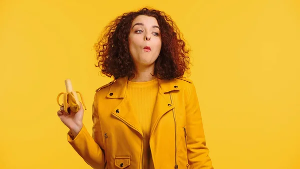 Mujer joven con chaqueta comiendo plátano aislado en amarillo - foto de stock