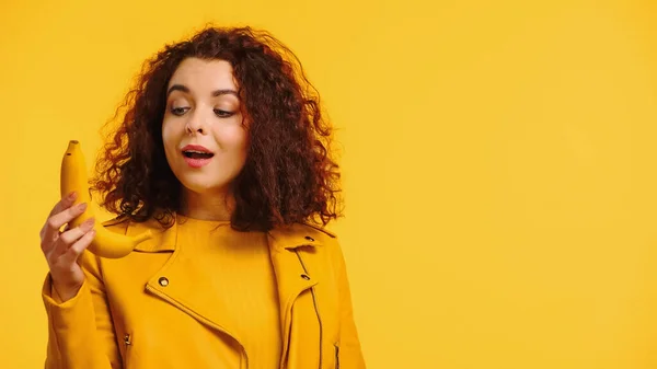 Curly woman looking at ripe banana isolated on yellow — Stock Photo