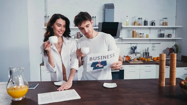 Hombre joven mostrando artículo en periódico de negocios a mujer sexy en camisa desabotonada - foto de stock