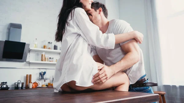 Young man embracing woman in white shirt on kitchen table — Stock Photo