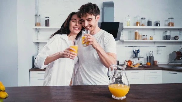 Jóvenes amantes felices bebiendo jugo de naranja fresco en la cocina - foto de stock