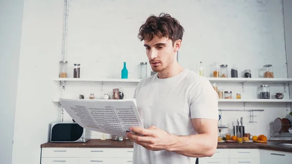 Jovem em branco t-shirt ler jornal na cozinha — Fotografia de Stock