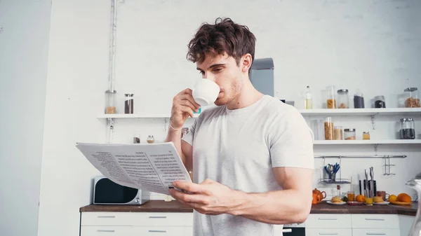 Man in white t-shirt reading newspaper while drinking morning coffee — Stock Photo