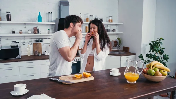 Couple of young lovers eating juicy orange in kitchen — Stock Photo