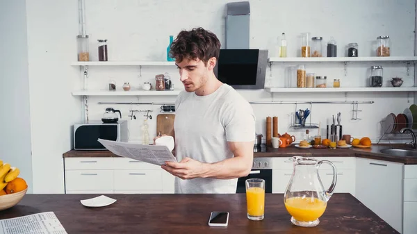 Homme en t-shirt blanc tenant une tasse de café tout en lisant le journal du matin — Photo de stock