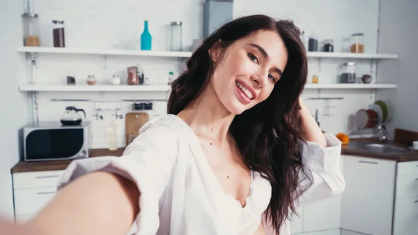 Sexy woman in white shirt smiling while taking selfie on blurred foreground — Stock Photo
