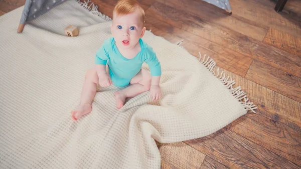 Высокий угол обзора младенца, сидящего на одеяле и смотрящего в камеру — стоковое фото