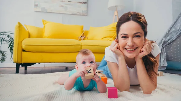 Happy mother looking at camera while infant son playing with toys — Stock Photo