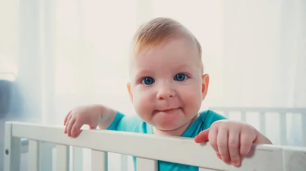 Junge mit blauen Augen blickt von weißer Krippe in die Kamera — Stockfoto