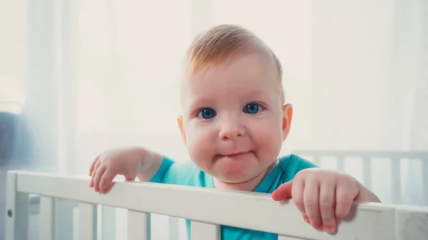 Baby boy with blue eyes looking at camera from white crib — Stock Photo