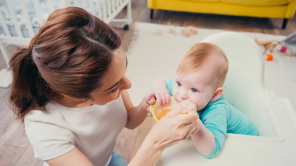 High angle view of brunette mother feeding infant son with baby food — Stock Photo