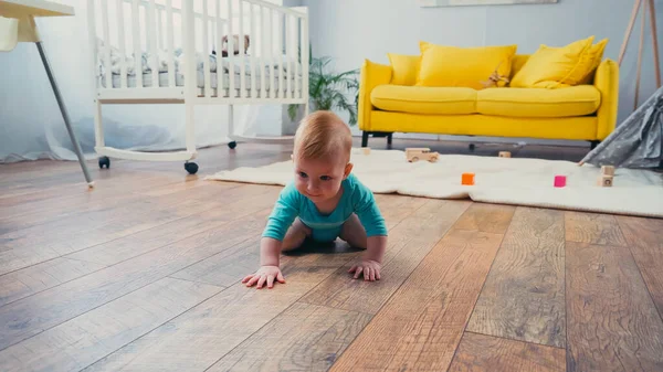 Infant boy in blue romper crawling on floor in living room — Stock Photo