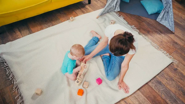 Вид зверху босоніж мати сидить біля немовляти син грає з іграшками — стокове фото