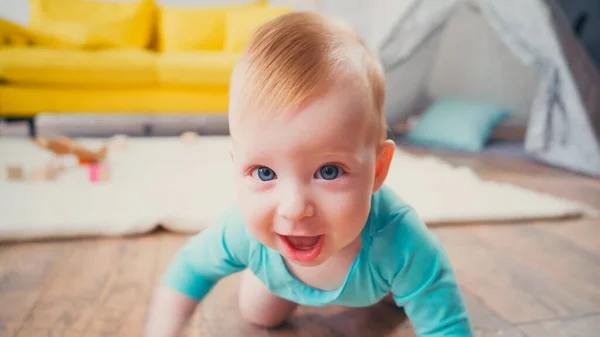 Happy infant boy with blue eyes looking at camera while crawling in living room — Stock Photo