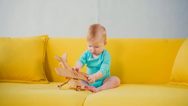 Baby boy sitting on sofa and playing with wooden biplane — Stock Photo