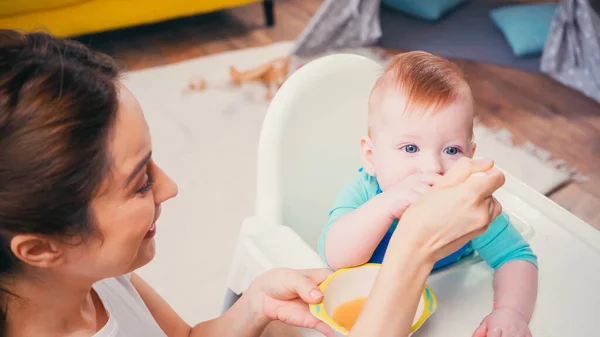 Mãe alegre alimentando filho bebê com comida de bebê — Fotografia de Stock