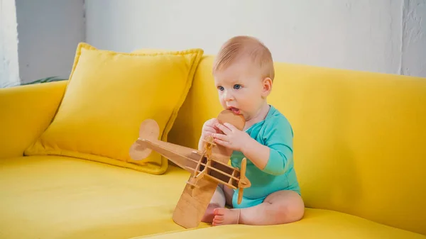 Мальчик сидит на диване и играет с деревянным бипланом — стоковое фото
