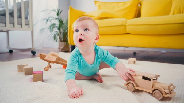 Мальчик с голубыми глазами сидит на одеяле и играет с деревянной игрушечной машиной — стоковое фото