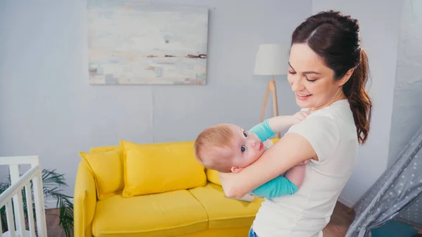 Cheerful mother nursing baby boy in living room — Stock Photo