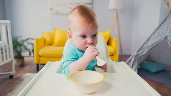 Bambino ragazzo seduto in alimentazione sedia e succhiare cucchiaio — Foto stock