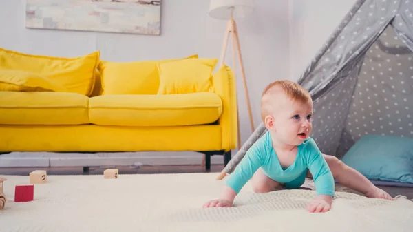 Säugling in blauem Strampler krabbelt auf Decke neben Tipi im Wohnzimmer — Stockfoto