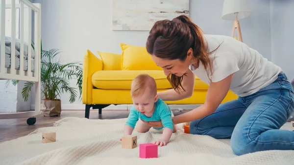 Happy mother looking at infant son playing with cubes on blanket — Stock Photo