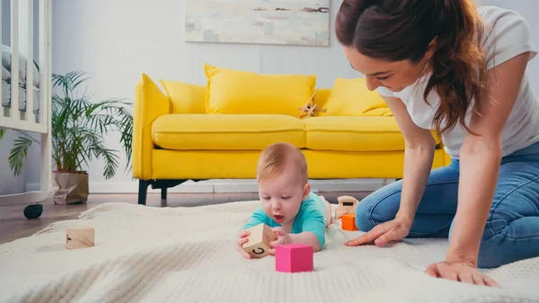 Веселая мать смотрит на младенца, играющего с кубом — стоковое фото