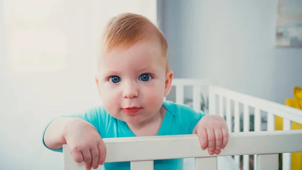 Мальчик стоит в детской кроватке и смотрит в камеру — стоковое фото