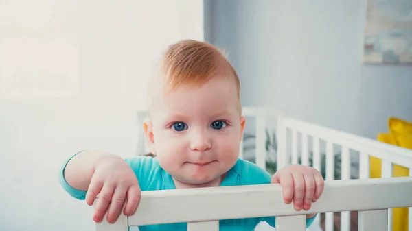Joyful infant boy standing in baby crib and looking at camera — Stock Photo