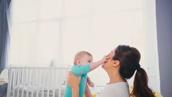 Bambino ragazzo raggiungere faccia di bruna madre vicino presepe — Foto stock