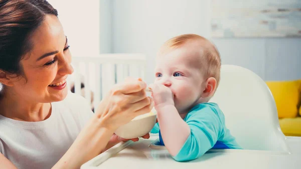 Alegre madre sonriendo mientras alimentación hijo bebé - foto de stock