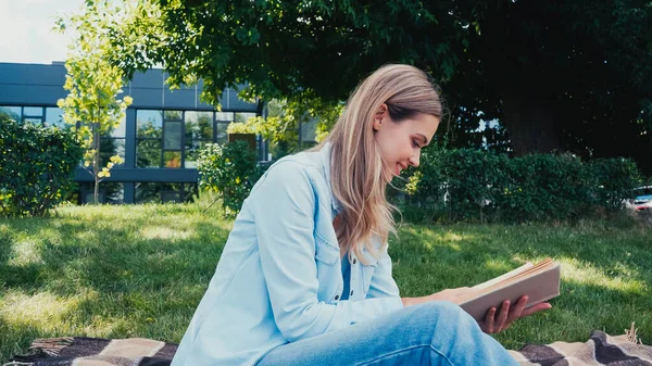 Вид сбоку веселой молодой женщины, читающей книгу в парке — стоковое фото