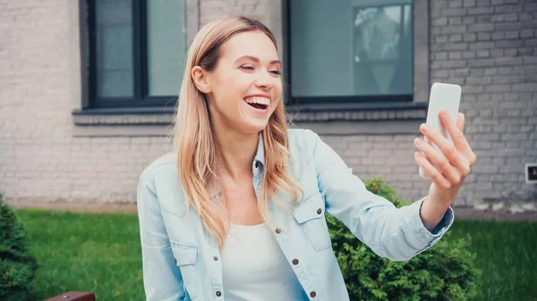 Fröhliche Studentin mit Videoanruf auf Smartphone in der Nähe von Gebäude — Stockfoto