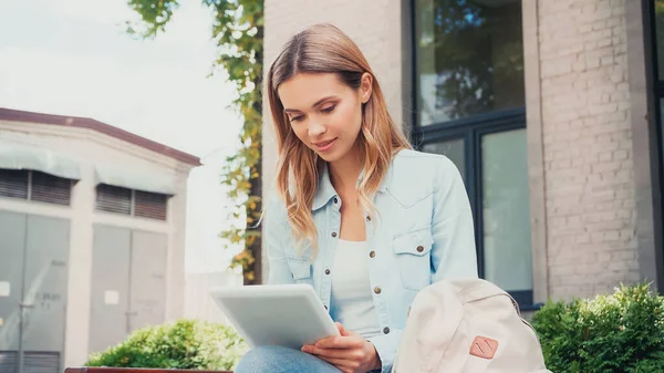 Pretty young student using digital tablet near building outside — Stock Photo