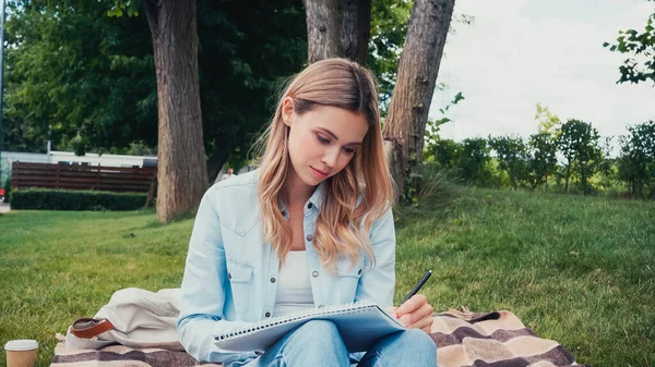 Jovem estudante escrevendo em notebook no parque — Fotografia de Stock