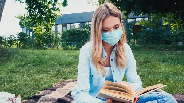 Student in medical mask reading book in park — Stock Photo